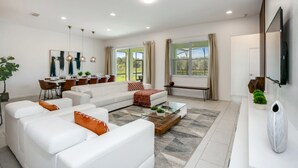 A modern living room with a white sofa set, a glass coffee table, and a dining area with a white table and chairs. - Villa in Solterra Resort 2764 (Davenport)
