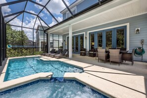 A swimming pool with lounge chairs and a hot tub area, surrounded by a covered patio with chairs and tables. - Villa in Reunion Resort & Spa 1346 (Kissimmee)