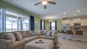 A modern living room with a beige sectional sofa, a coffee table with a book, and a ceiling fan. - Villa in Solterra Resort 1510 (Davenport)