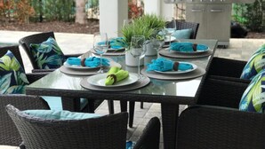 An outdoor dining area with wicker chairs and tables, a grill, and potted plants.