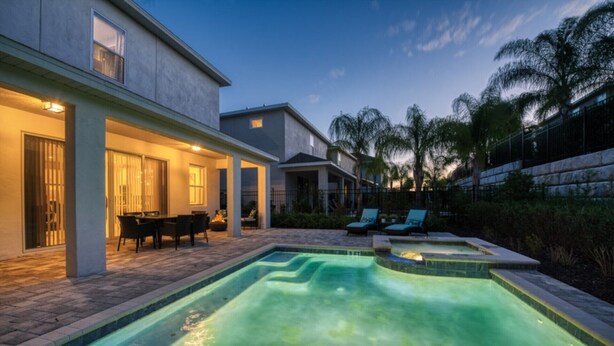 A modern house with a swimming pool, outdoor seating, and a well-lit patio area.