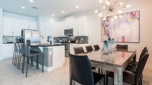 A modern kitchen with white cabinets, a central island, and a dining area with a glass table and black chairs.