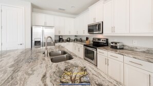 A modern kitchen with white cabinets, stainless steel appliances, and a marble countertop. - Villa in Encore Resort at Reunion 2985 (Kissimmee)