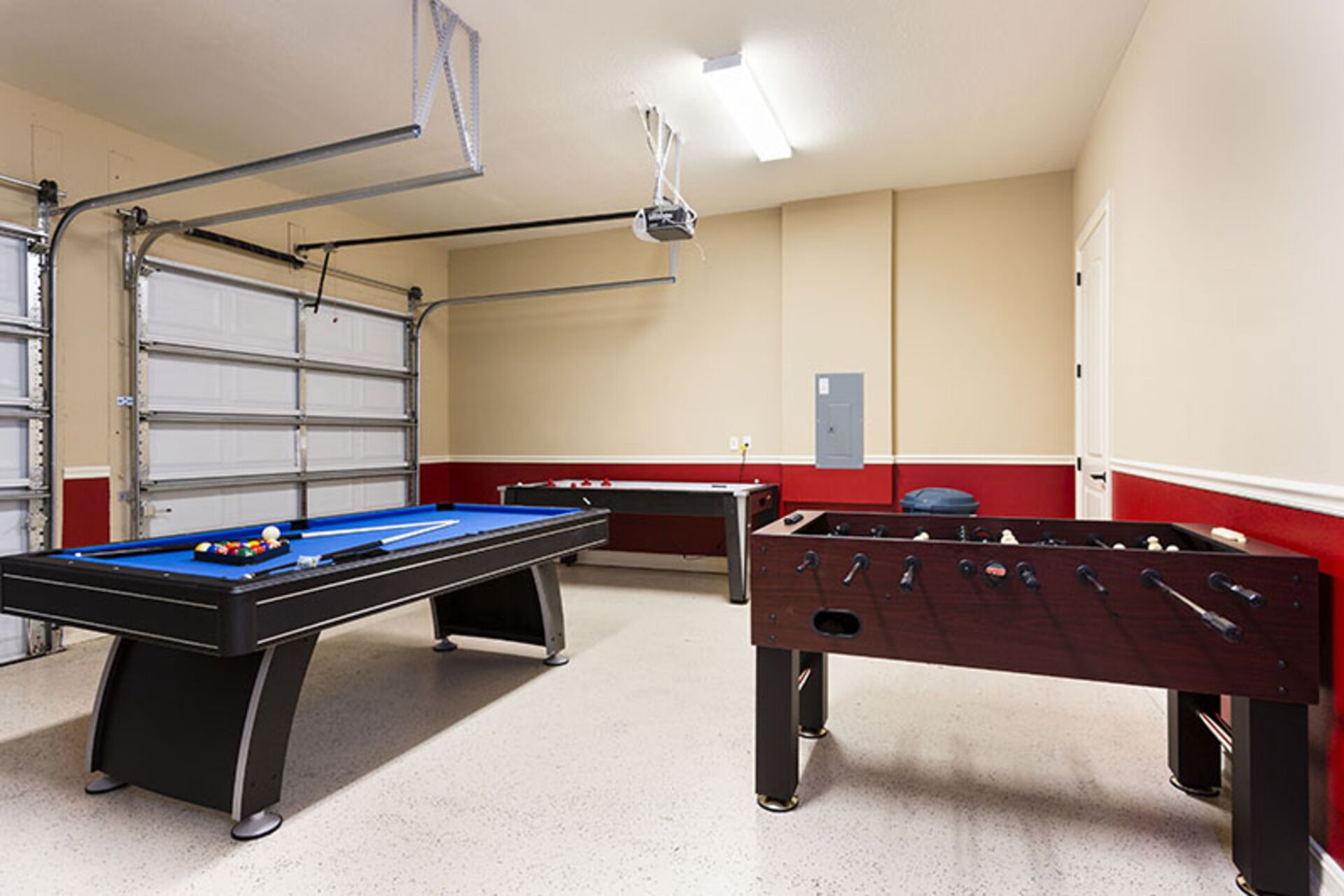 Une table de billard, une table de baby-foot et une porte de garage dans une pièce aux murs de couleur beige et aux bordures rouges.
