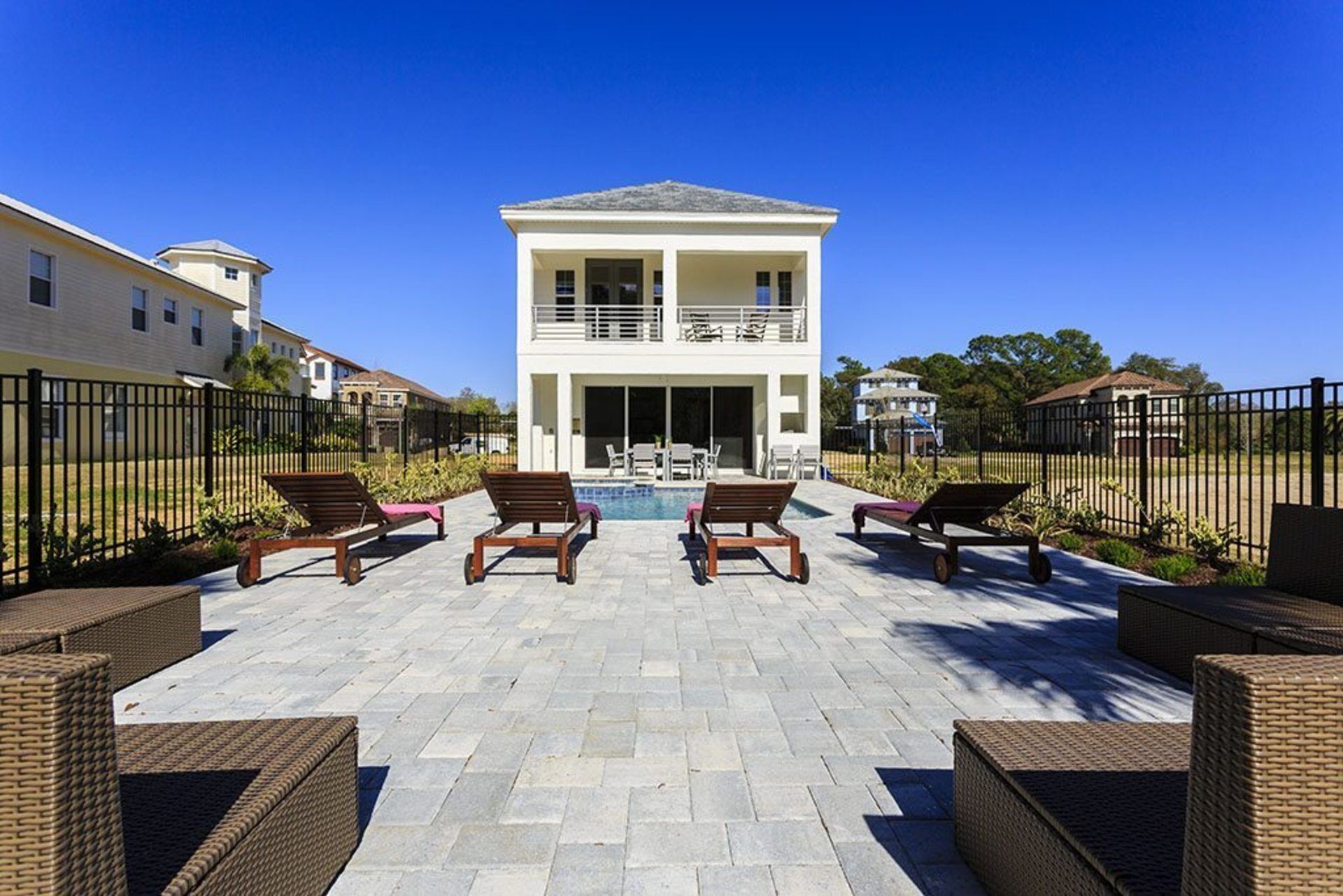 A two-story house with a swimming pool in the backyard, surrounded by a fence and outdoor furniture.