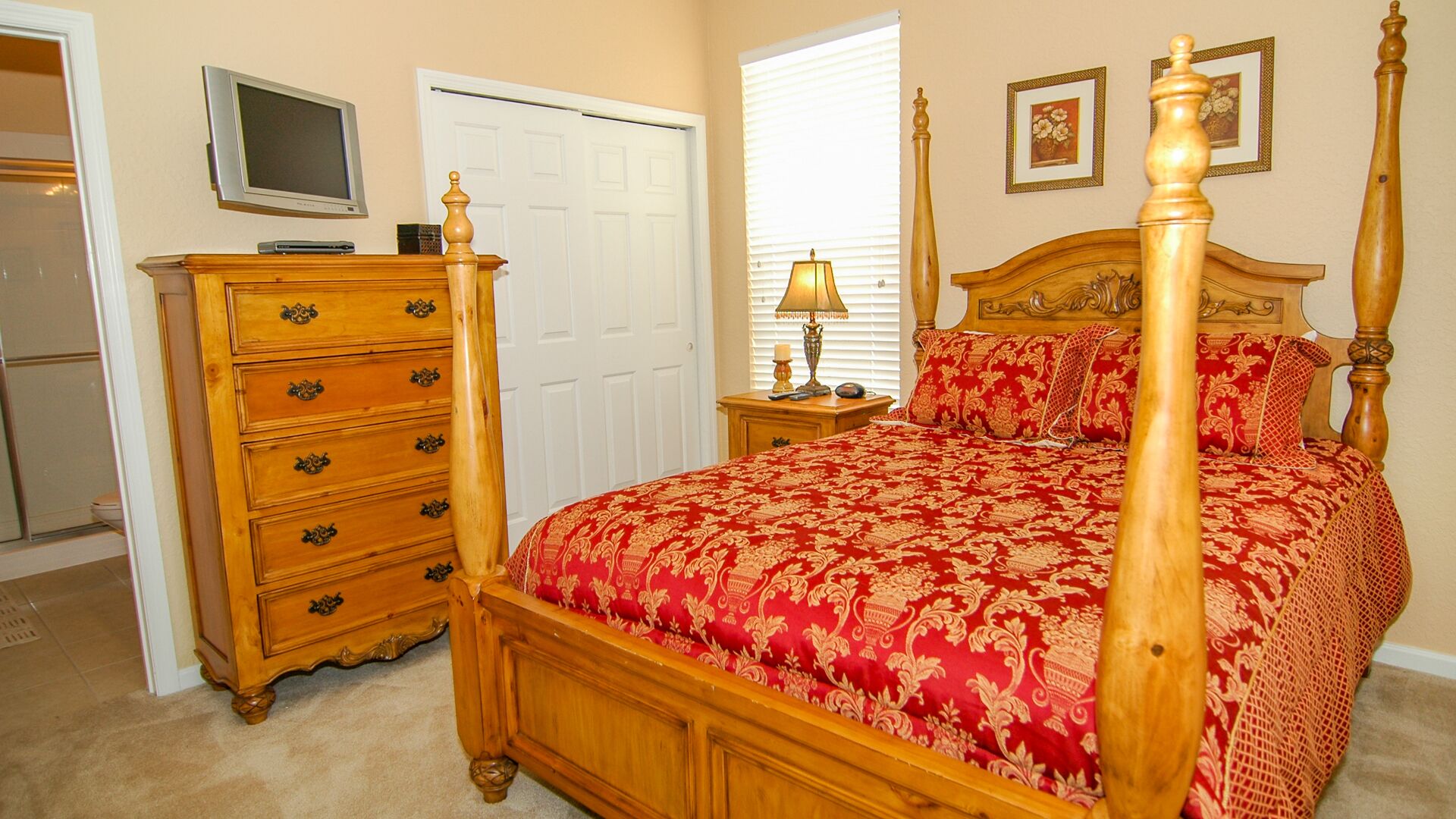 Un dormitorio con cama con dosel, cómoda de madera, televisor y ventana con persianas.