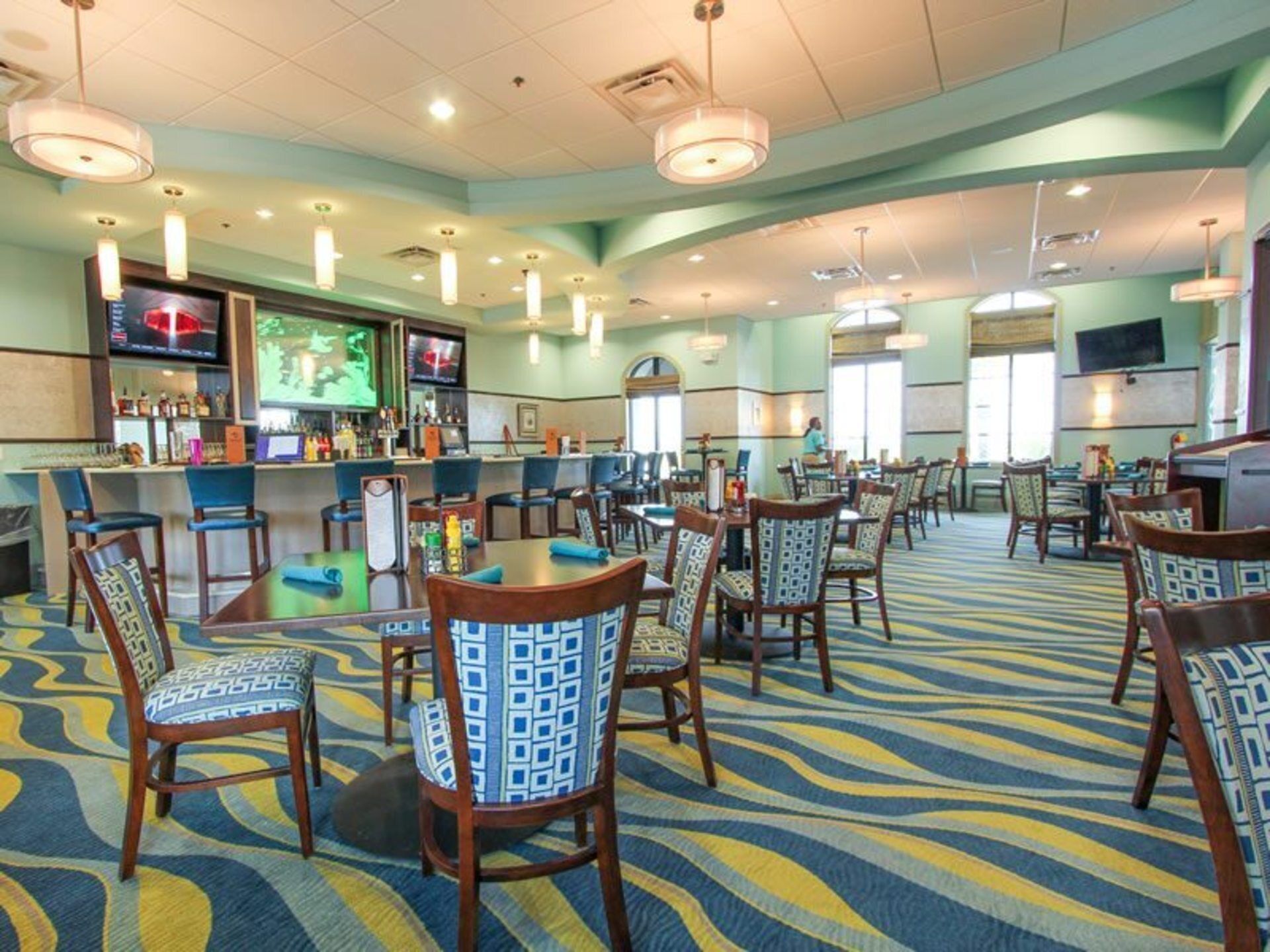 A hotel lobby with a bar area, multiple seating arrangements, and a patterned carpet.