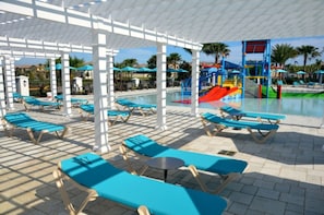 A poolside area with sun loungers and umbrellas, a children's play structure, and a clear view of the pool. - Villa in Windsor at Westside Resort 1769 (Kissimmee)