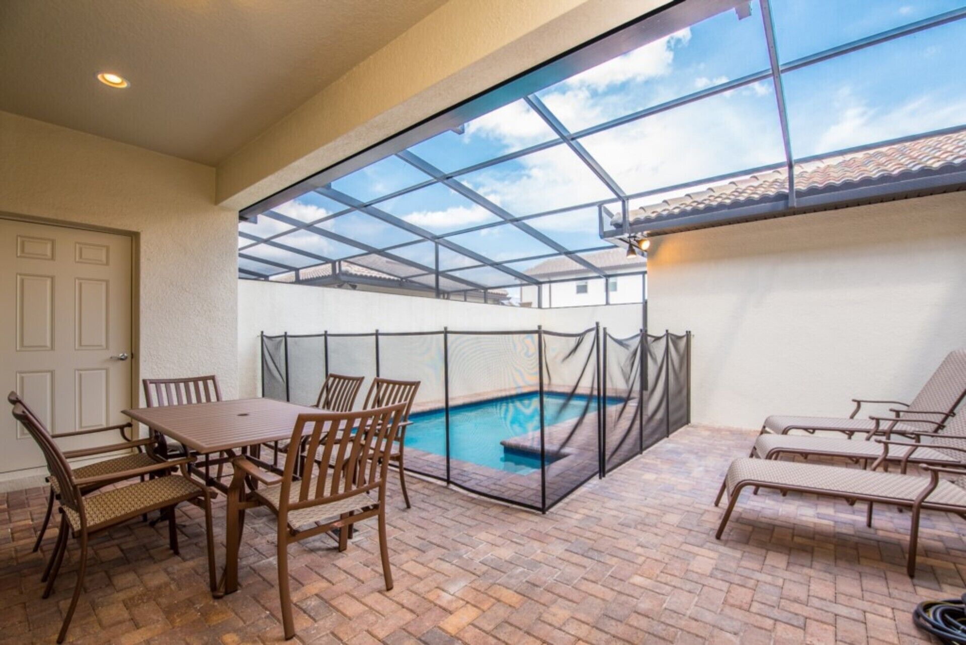 Een overdekt terras met een zwembad, tuinmeubels en een glazen dak.