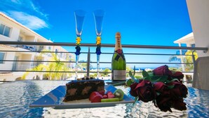 A table with a slice of cake, a bottle of champagne, and a bouquet of roses on a balcony overlooking a coastal area. - Beautiful Apartment With Communal Pool, Protaras Apartment 1287 (Paralimni)