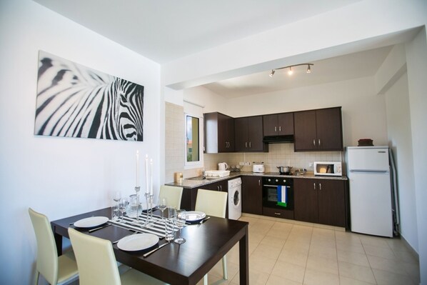 A modern kitchen with dark cabinets, a white refrigerator, and a dining area with a table set for four.