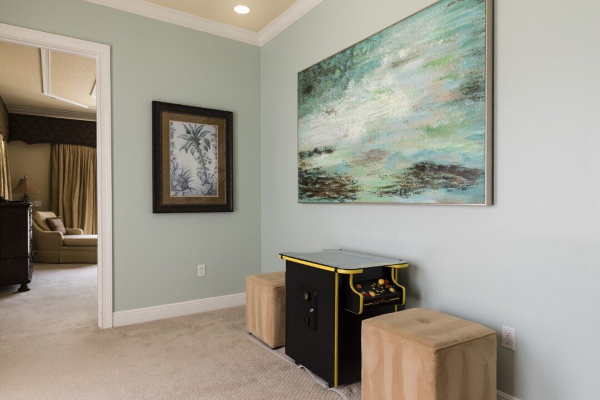Una habitación con una obra de arte floral enmarcadas, un cuadro abstracto grande y una pequeña mesa negra con detalles amarillos.