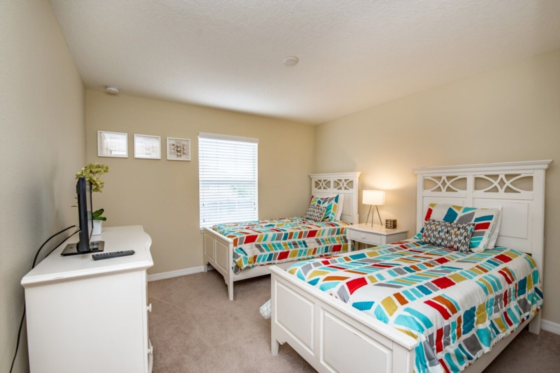 A bedroom with two beds, a desk, and a window with blinds.