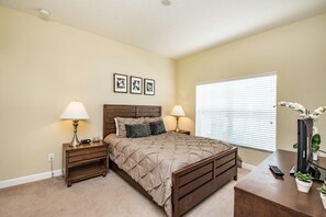 A bedroom with a bed, two bedside tables, a nightstand, a dresser, a window with blinds, and a wall-mounted TV. - Townhome in Champions Gate Resort 2827 (Kissimmee)