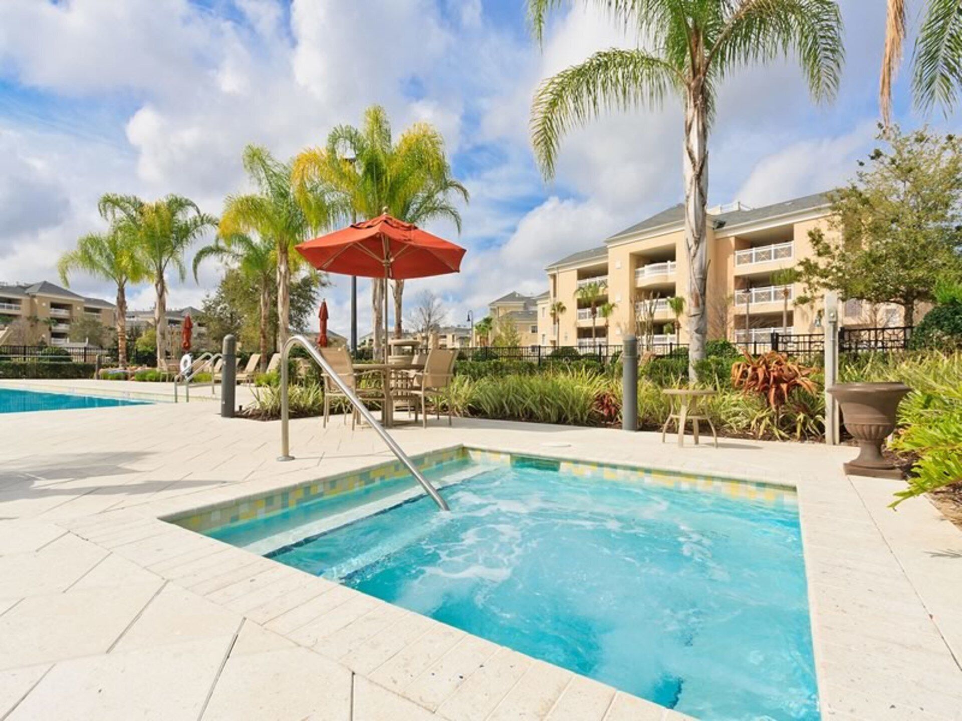 A swimming pool with a red umbrella, palm trees, and a building in the background.