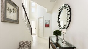 A hallway with a staircase, a framed picture, a mirror, a console table with a plant, and a patterned bench. - Villa in Reunion Resort & Spa 1362 (Kissimmee)
