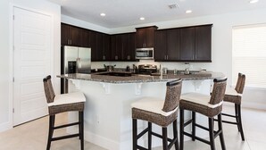 A modern kitchen with dark wood cabinets, stainless steel appliances, and a central island with bar stools. - Villa in Reunion Resort & Spa 1362 (Kissimmee)