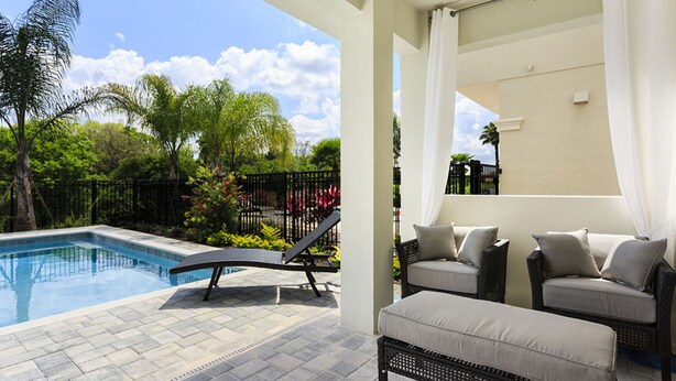 A pool area with a lounge chair and ottoman, surrounded by greenery and a fence. - Villa in Reunion Resort & Spa 1362 (Kissimmee)