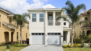 A two-story residential building with a central garage, surrounded by palm trees and a well-maintained lawn. - Villa in Reunion Resort & Spa 1362 (Kissimmee)