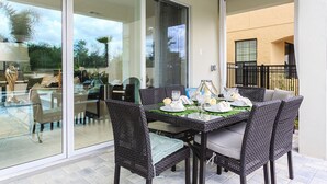 A dining area with a glass table and wicker chairs, a sliding glass door leading to a patio, and a view of a building in the background. - Villa in Reunion Resort & Spa 1362 (Kissimmee)