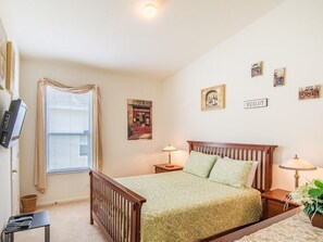 A bedroom with a single bed, a bedside table with a lamp, a wall-mounted TV, and a window with curtains. - Villa in Windsor Palms Resort 1032 (Kissimmee)