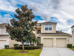 A two-story house with a garage, a tree in the front yard, and a clear sky. - Villa in Windsor Hills Resort 1093 (Kissimmee)