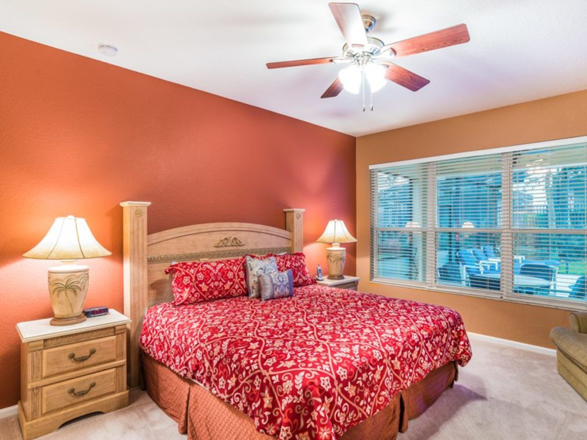 A bedroom with a bed, two bedside tables with lamps, a ceiling fan, and a window with blinds.