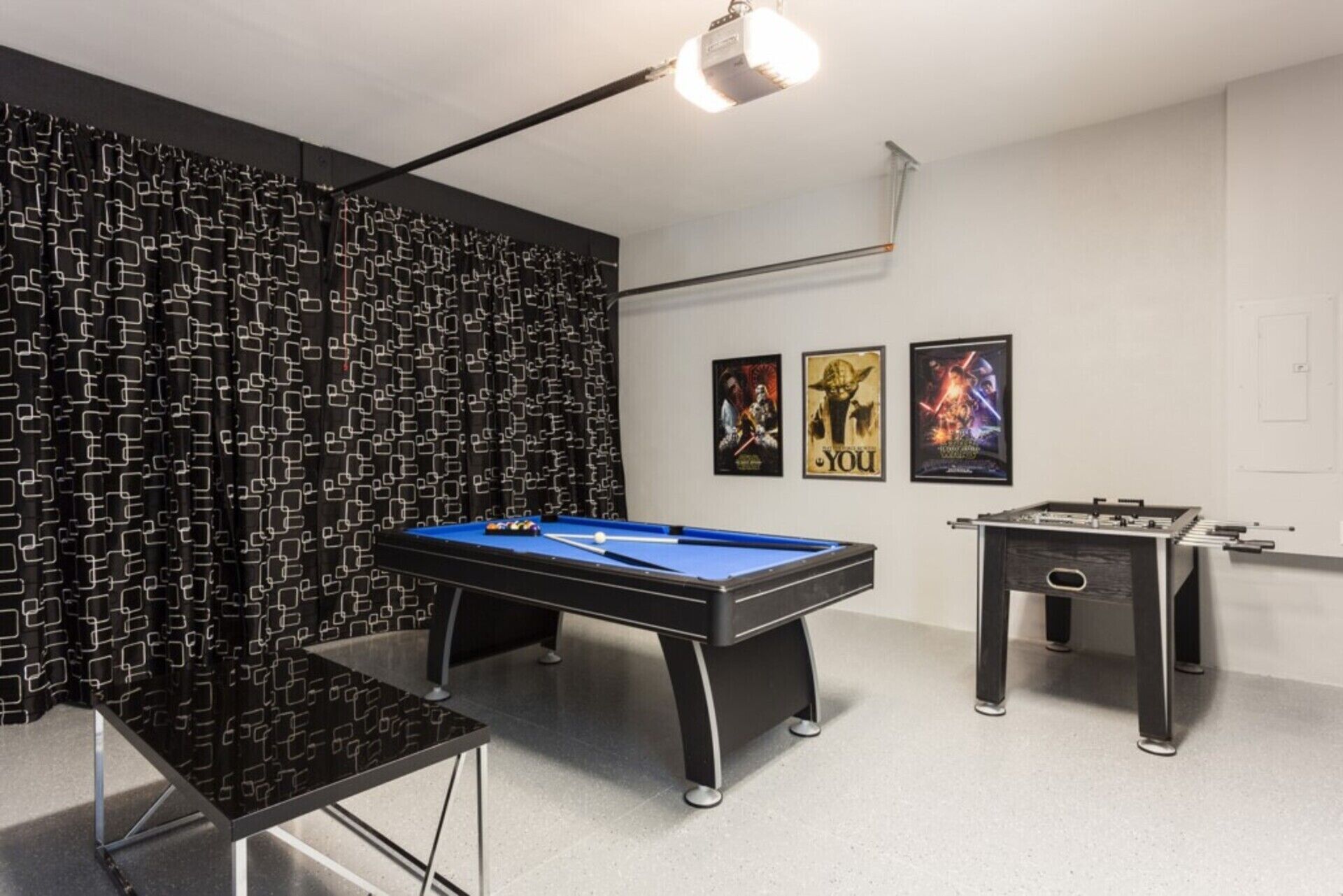 A room with a pool table, a foosball table, and two posters on the wall.