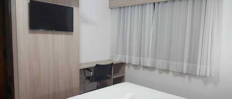 A hotel room with a bed, a desk, a chair, a TV, and a window with curtains.