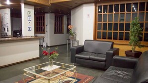Un vestíbulo con mostrador de recepción, un sofá de cuero negro, una mesa de centro de vidrio con un jarrón de flores y un ventanal con persianas.