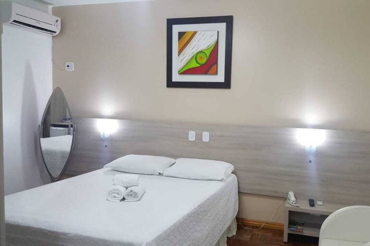 Une chambre d’hôtel comprenant un lit, une table de chevet, un miroir, un tableau encadré et un climatiseur fixé au mur.