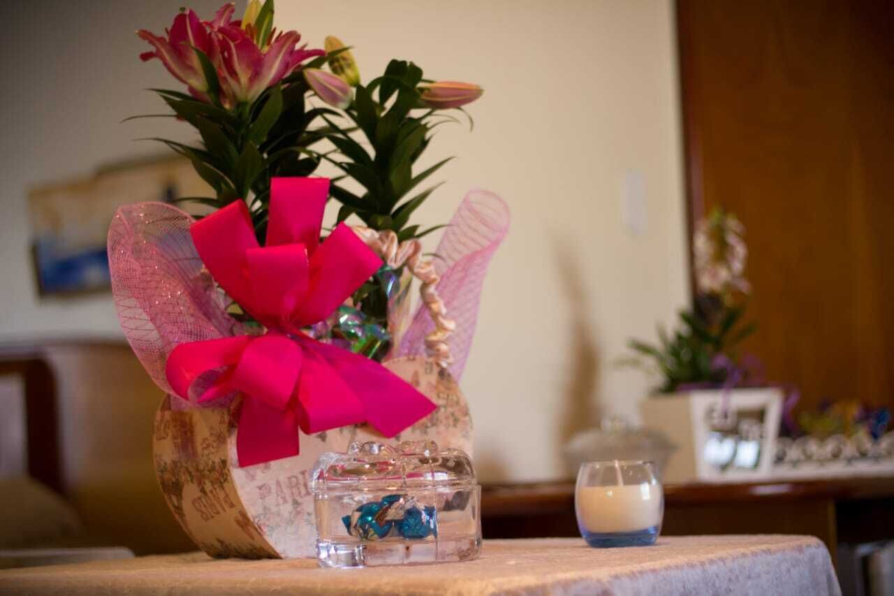A decorative arrangement with a pink bow, a clear glass container with blue objects, and a candle on a wooden surface.