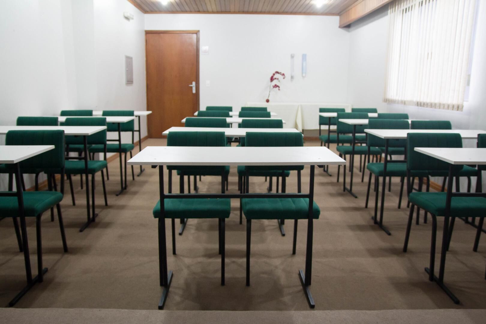 Un salón de conferencias con sillas verdes y mesas blancas dispuestas en filas.