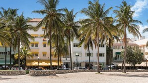Ein Hotel mit gelber Fassade, Palmen und einer Sandstrandanlage.