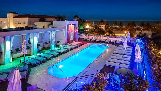 Ein Poolbereich mit Liegestühlen und Sonnenschirmen, ein Pool und Meerblick bei Nacht.