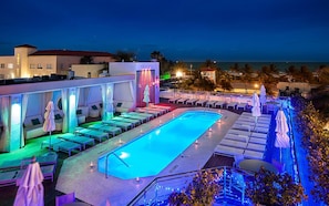 Uma área à beira da piscina com espreguiçadeiras e guarda-sóis, uma piscina e vista para o oceano.