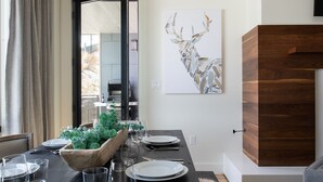 Un comedor con una mesa de madera dispuesta para cuatro, un espejo grande y un ciervo como decoración en la pared.