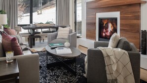 Una sala de estar moderna con chimenea, asientos cómodos, un comedor y un ventanal con vistas a un paisaje nevado.