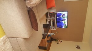 A living room with a sofa, a television, a bookshelf, and a small table with decorative items. - By Grace apartment near sportman arms,hosted by regina (Nanyuki)