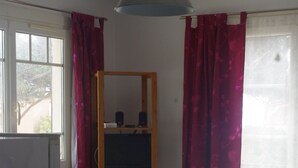 A dining area with a table covered in a patterned tablecloth, surrounded by chairs. A wooden shelf unit with electronic equipment is visible in the background. - T2 1st floor of the villa of the sea (Hyères)