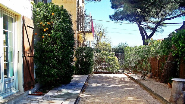 A narrow paved pathway flanked by greenery and a building with a window and a door. - T2 1st floor of the villa of the sea (Hyères)