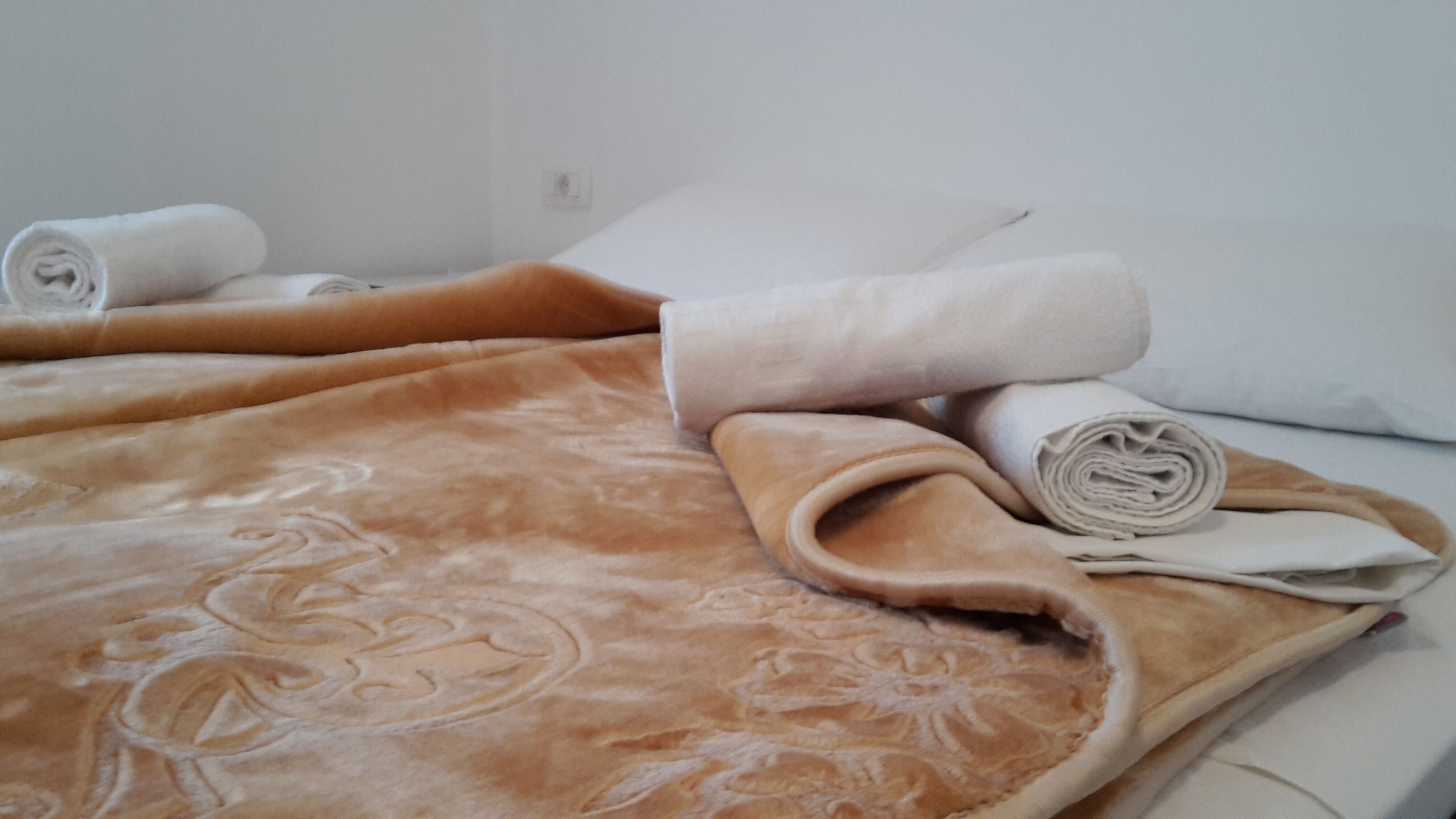 A bed with a brown blanket and rolled towels.