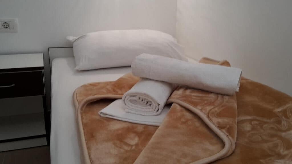 A neatly made bed with a brown blanket and rolled white towels.