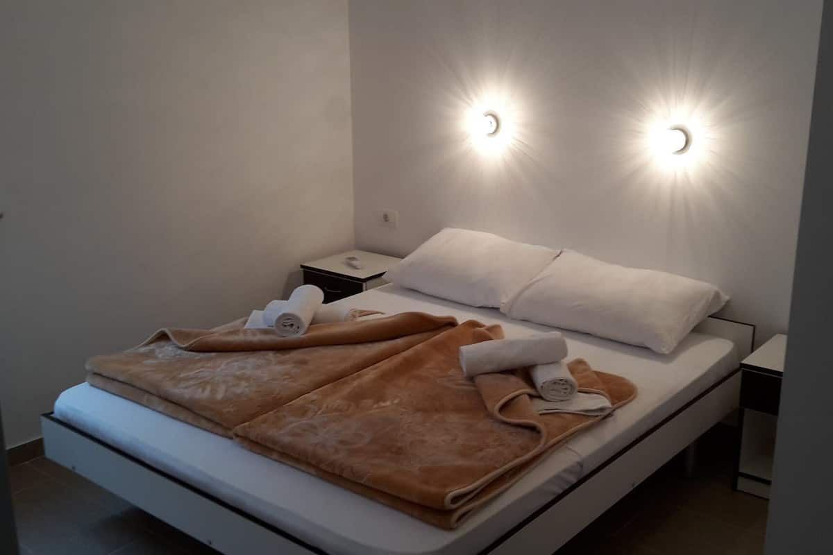 A modern hotel room with a bed, two bedside tables, and wall-mounted lights.