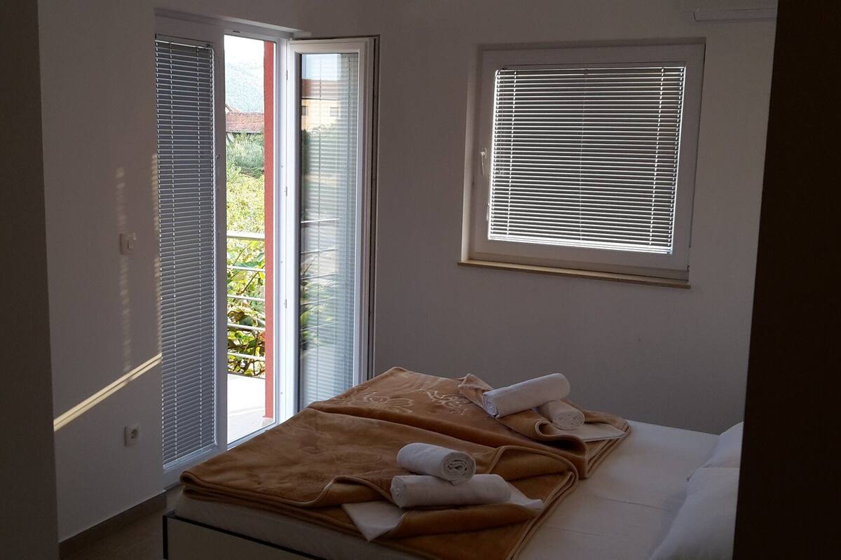 A bedroom with a bed, a window with blinds, and a door leading to an outdoor area.