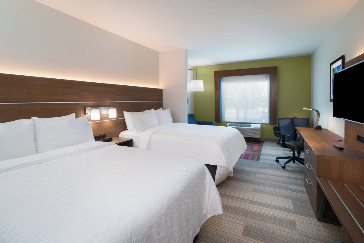 A hotel room with two beds, a desk, a chair, a TV, and a window with a view.