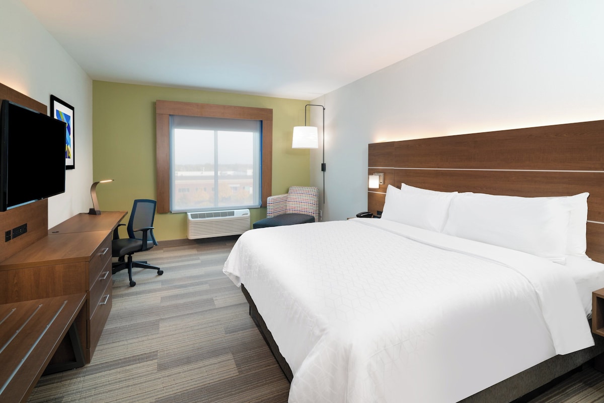 A hotel room with a bed, a desk, a chair, a television, and a window.