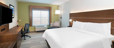 Quarto de hotel com cama, escrivaninha, cadeira, televisão e janela.