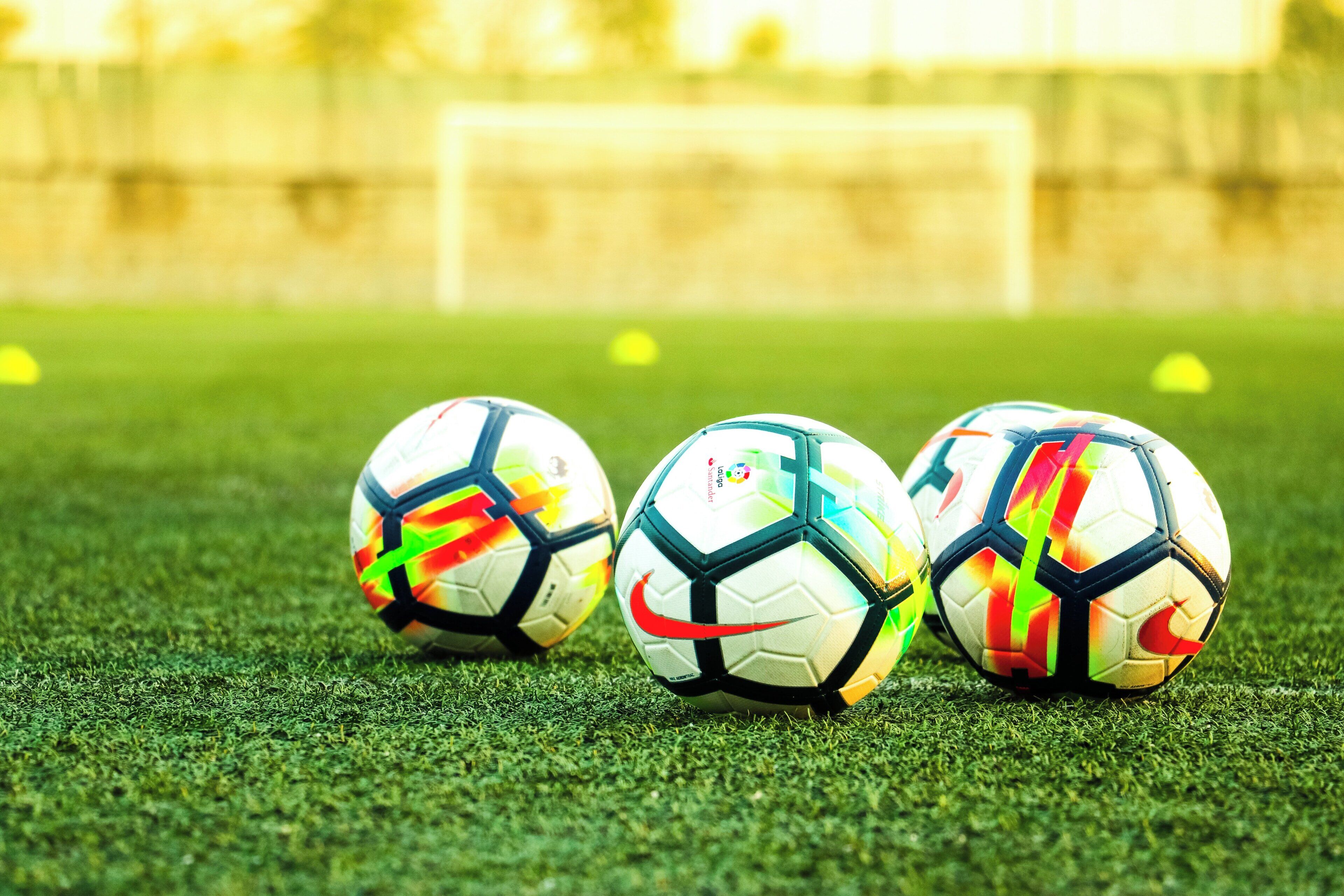 Tres balones de fútbol sobre un campo de césped con un fondo desenfocado.