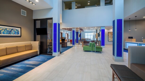 A spacious lobby with a high ceiling, a reception desk, seating areas, and a staircase leading to an upper level. - Holiday Inn Express & Suites St Peters by IHG (St. Peters)